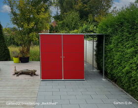 Ein roter Gartenschrank auf einer Terrasse mit einem großen Reptil davor, umgeben von Pflanzen und Bäumen.