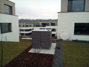 . Ein moderner Gartenhof mit Gebäude im Hintergrund, trübem Himmel und einigen verstreuten Gegenständen am Boden.