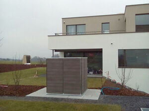 . Moderne Gebäude mit Garten, Rasen, Kiesweg und Holzelementen im Vordergrund an einem bewölkten Tag.