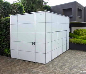 Moderner Gartenschuppen neben einem Haus, umgeben von Pflanzen.