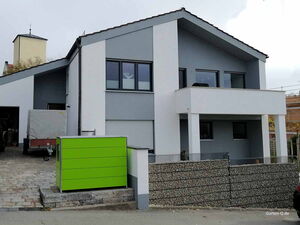. Modernes Haus mit grauer Fassade, grünem Gartenschrank und gepflasterter Auffahrt.