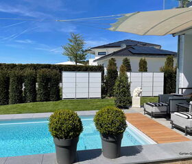 Ein moderner Garten mit Pool, Sonnensegel, Büschen, Sitzecke und einer Skulptur.