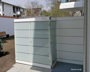 Ein moderner Gartencontainer neben einem Gebäude, umgeben von Terrasse und Gartenbereich mit Bank.