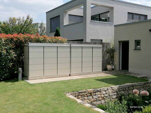 . Moderner Gartenschrank neben einem Haus in einem gepflegten Garten mit Rasen und Steinmauer.