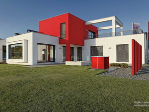 . Modernes Gebäude mit weiß-roter Fassade, großen Fenstern und gepflegtem Rasen im Vordergrund.