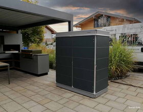 Garten mit überdachtem Grillbereich, modernem Schrank und Holzhäusern im Hintergrund.