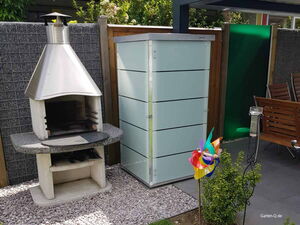 . Grill und Gartenschrank neben Gartenmöbeln und Windrad in einem Garten.