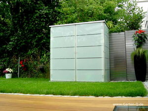 . Ein moderner Gartenschrank mit Glasfronten steht auf Rasen, umgeben von Pflanzen und Holzboden.