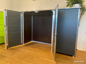 . Grauer Schrank mit drei geöffneten Türen, Holzfußboden, Pflanze oben.