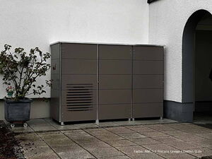 . Metallschrank neben Hauswand, Pflanze im Topf links, graue Bodenfliesen.