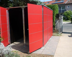 . The image shows a red outdoor structure with open doors, possibly a garbage or recycling bin enclosure. It seems to be made of panels with metal framing, located outdoors with some vegetation and a house in the background.