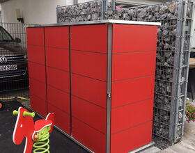 . The image shows a red storage unit next to a galvanized metal structure filled with rocks, possibly for support or decoration. There's also a small children's playground spring rider in the shape of a horse in the foreground. A parked vehicle is visible in the background, along with a covered area or carport.
