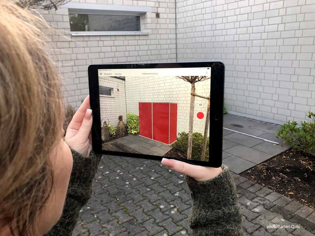 Eine Person hält ein Tablet mit einem Bild eines roten Schranks in einem Hof.