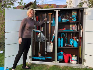 . Frau vor Gartenwerkzeugschrank mit Schaufeln, Rechen, Gießkanne und anderen Gartenutensilien.