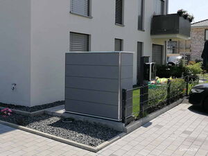 . Ein grauer Geräteschrank neben einem modernen Wohnhaus im Gartenbereich.