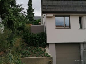 . Haus mit Dachfenstern, Garage und Garten voller Pflanzen und Bäume.