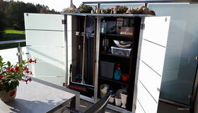 Ein offener Gartenschrank mit Reinigungsutensilien und Blumentöpfen auf einem Balkon.