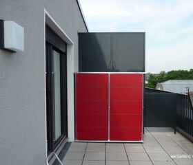 . Ein roter und schwarzer Schrank auf einem Balkon mit grauen Wänden und Geländer.