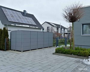 Ein modernes Haus mit Solarpanelen, graue Gartenschränke, gehwegartiger Boden, etwas Schnee, kahle Bäume und Sträucher.