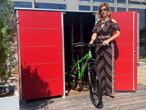. Frau mit Sonnenbrille holt ein grünes Fahrrad aus einem roten Schuppen.