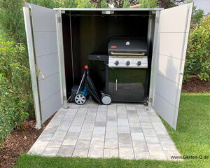 The image shows a storage unit with open doors. Inside, there is a barbecue grill and a lawn mower. The unit is placed on a tiled patio, surrounded by grass and shrubs.