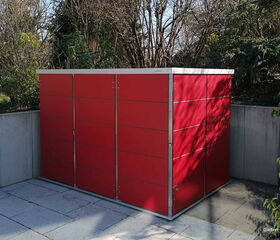 . Ein rotes Gartenhaus steht auf einer gepflasterten Terrasse, umgeben von Bäumen und Sträuchern.