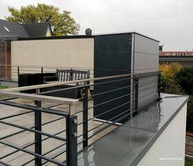 Eine moderne Dachterrasse mit Geländer und Sitzbereich, umgeben von Bäumen und Gebäuden.