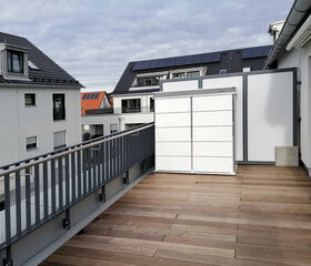 Eine moderne Dachterrasse mit Holzboden, Geländer und Blick auf benachbarte Gebäude, einige mit Solarpanels auf den Dächern.