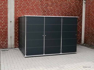 . Ein grauer Gartenschrank vor einer roten Ziegelmauer auf grauen Fliesen.