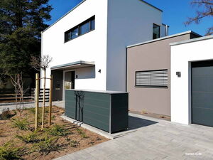 . Modernes Haus mit Flachdach, großem Fenster und gepflegtem Gartenbereich, umgeben von Bäumen und Steinweg.