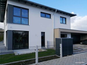 . Modernes zweistöckiges Haus mit Garage, großen Fenstern, Zaun und gepflasterter Einfahrt.