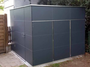 . Ein graues Gartenhaus mit flachem Dach, stabilem Design und 200 cm Höhe. Umgebung: Pflastersteine, Zaun und Bäume.