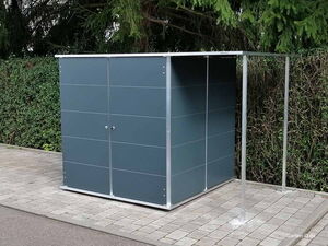 . Ein moderner grauer Gartenschuppen mit Metallrahmen steht auf Pflastersteinen neben einer Hecke.