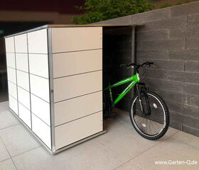 . Ein Fahrrad steht teils in einem modernen, weißen Schuppen mit Steinwandhintergrund.