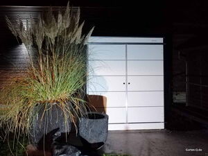 . Ein großer Pflanzenkübel mit Gras vor einem modernen weißen Schuppen.