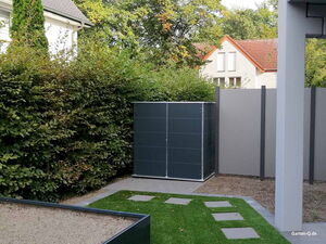 . Ein moderner Garten mit Rasen, Pflastersteinen, Hecke und einem schwarzen Schuppen.