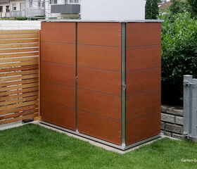 . Ein brauner Gartenschrank auf grünem Rasen, daneben ein Holzzaun und ein Gitterzaun.