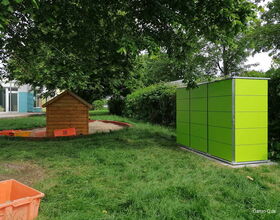 . Ein grüner Schuppen, Sandkasten mit Häuschen und Bäume in einem Garten.