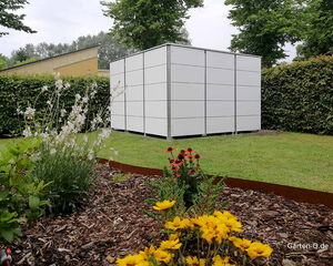 . Ein moderner Gartenschuppen auf einer Wiese, umgeben von Blumen und Hecken.