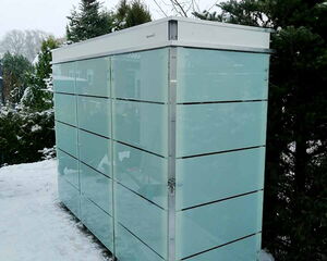 Ein moderner, rechteckiger Gartenschrank aus Glas steht auf einem schneebedeckten Boden, umgeben von Bäumen.