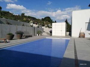 . Moderner Garten mit Pool, Terrasse, Pflanzen, Bank und weißem Schuppen.