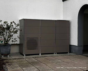 . Metallschrank neben Hauswand, Pflanze im Topf links, graue Bodenfliesen.