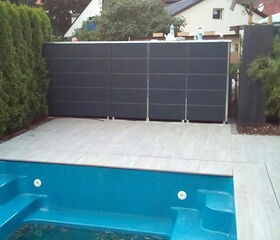 Leerer blauer Pool im Garten mit bepflanzten Hecken, Fliesenboden und Sichtschutzwand.