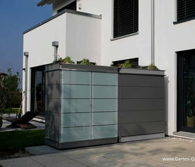 . This image features a modern, minimalist outdoor storage cabinet situated on a patio. The cabinet has a sleek design with a combination of glossy and matte surfaces. It is positioned against the wall of a contemporary house. Surrounding elements include some garden plants and a lawn area, providing an overall neat and organized look to the outdoor space.