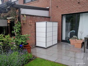 . Eine Terrasse mit Pflanzgefäßen und einem modernen, weißen Garten-Schrank an einer Backsteinwand.