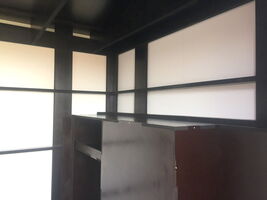 The image appears to show a room with a modern, minimalist design. It features a geometric pattern created by horizontal and vertical black beams against light panels, resembling a grid. There's a dark-colored structure or piece of furniture in the corner. The overall aesthetic gives a clean, organized appearance.