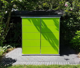 . The image shows a garden storage unit with a bright green color. It has a modern, minimalist design with a sleek, rectangular shape and paneling. The unit is situated on a paved area with greenery and trees surrounding it.