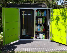 Here's a breakdown of the image contents in array format:

- **Left Section:**
  - Open green door
  - Shovel
  - Rake or broom
  
- **Middle Section:**
  - Shelves with various boxes and containers
  - Bottles
  - Buckets

- **Right Section:**
  - Open green door
  - Gardening supplies
  - Umbrella (or similar item)

- **General:**
  - Outdoor storage area or shed
  - Brick or stone ground
  - Surrounded by greenery and trees

Let me know if you need more information!