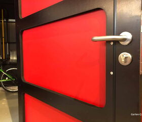 . Roter Türrahmen mit silbernem Griff, im Hintergrund ein grünes Fahrrad in der Garage.