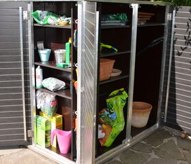 . The image shows a storage cabinet with multiple shelves. Here's a breakdown of the contents:

1. **Top Shelf:**
   - Various small bags, possibly with gardening materials.
   - Some items in containers.

2. **Middle Shelves:**
   - A metal bucket.
   - A green bottle.
   - Various gardening tools and materials, such as seeds and plant pots.

3. **Bottom Shelf:**
   - Cans and small bags.
   - A pink watering can.
   - Larger bags, possibly potting soil or fertilizer.

4. **Right Section:**
   - More bags, potentially soil or compost.
   - Clay pots and trays.

This setup appears to be for gardening supplies and tools.